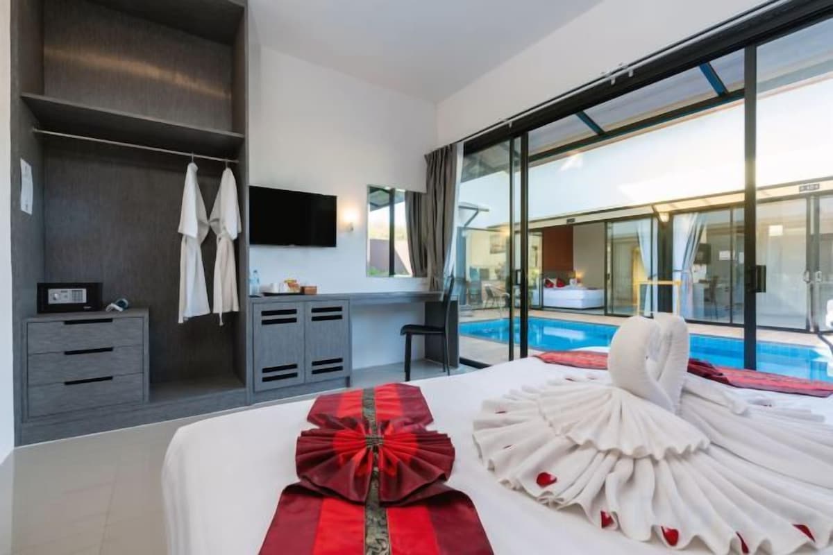 A hotel room with a bed, a desk, a chair, a TV, a wardrobe, and a view of a swimming pool.