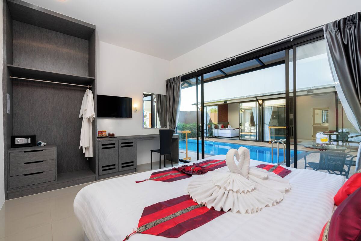 A hotel room with a large bed, a desk, a chair, a TV, and a view of a swimming pool.