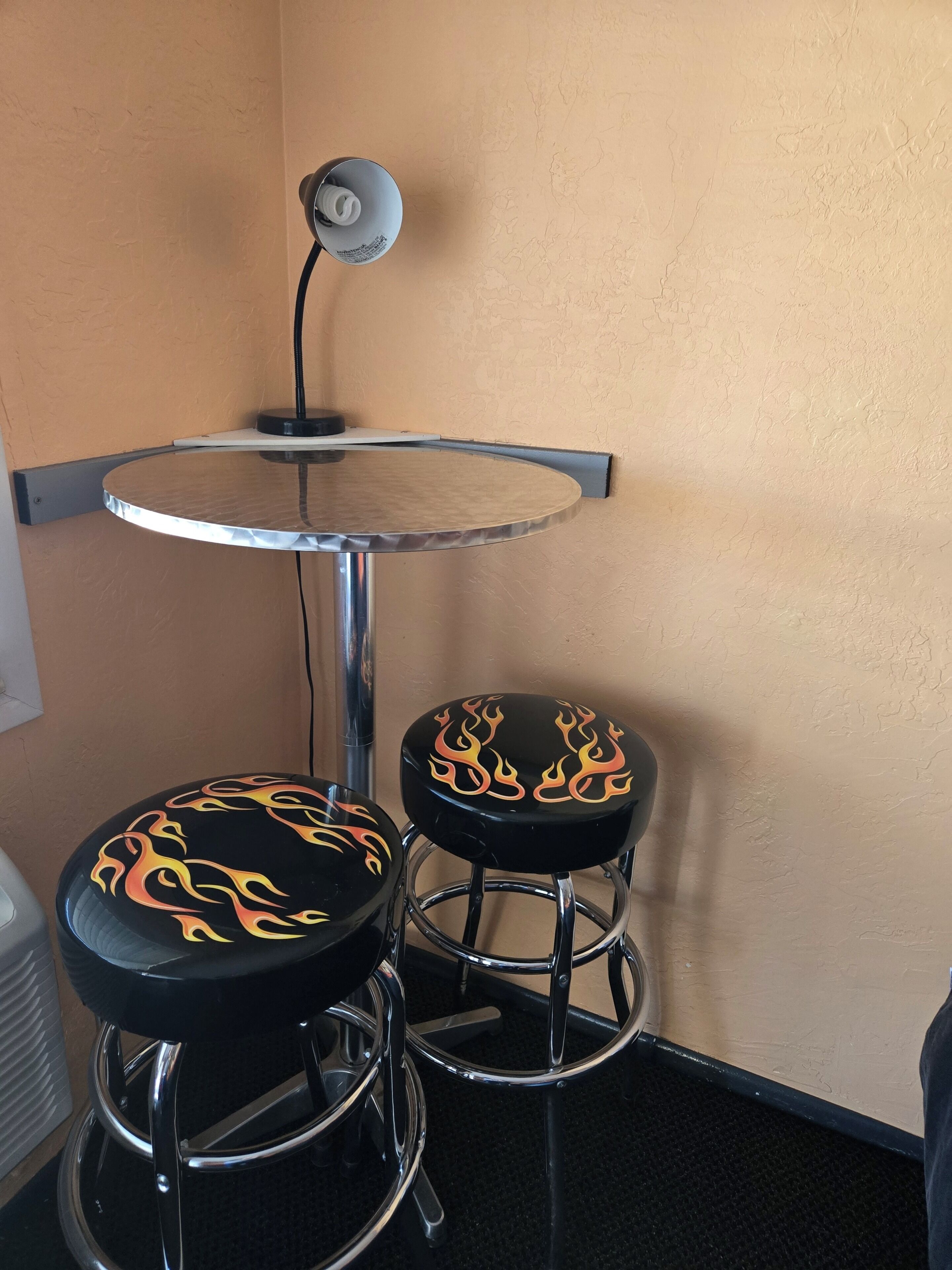 Una habitación de esquina con una pequeña mesa redonda y dos taburetes negros decorados con diseños de llamas.