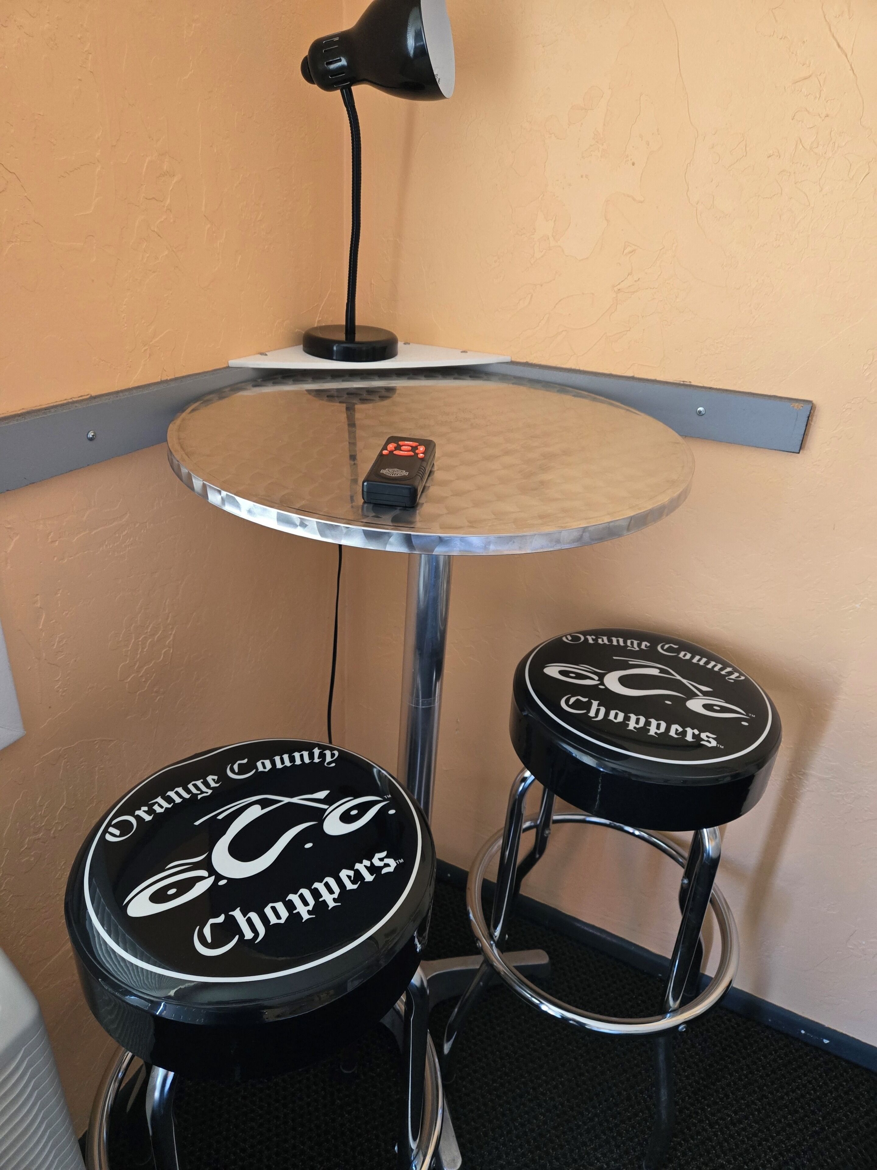 A corner with a round table, two stools, a lamp, and a wall-mounted object.