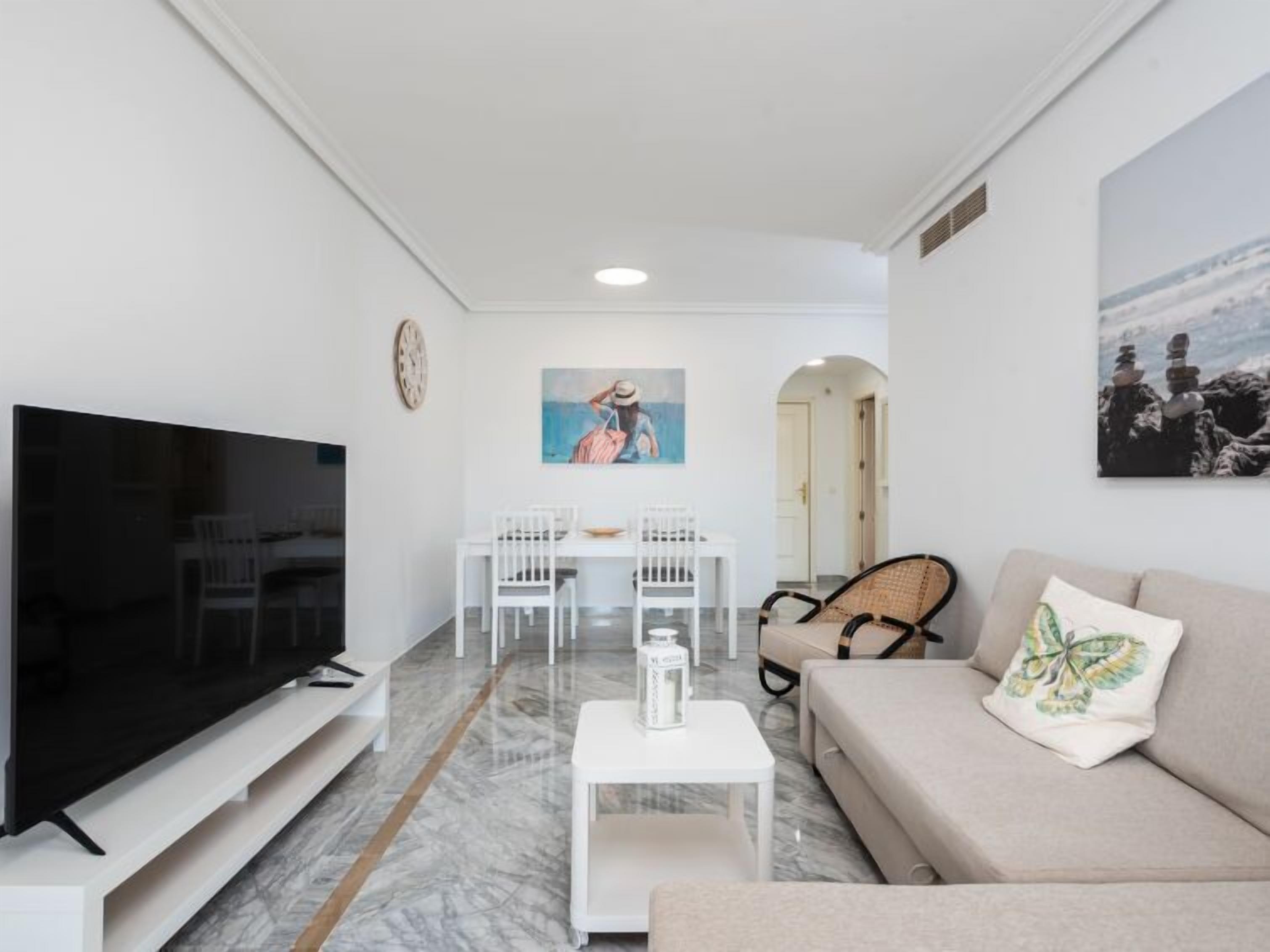 A living room with a flat-screen TV, a sofa, a coffee table, and a dining area with chairs and a table.