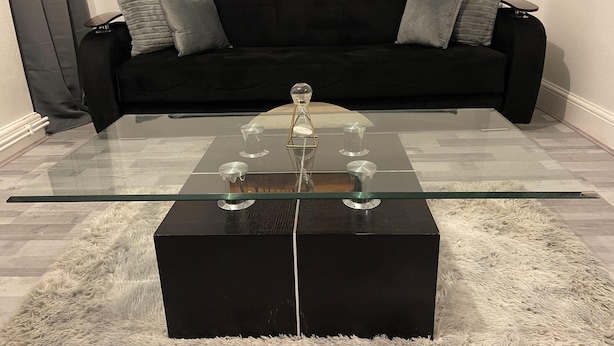Un salon moderne avec une table basse en verre, un canapé noir et des coussins gris.