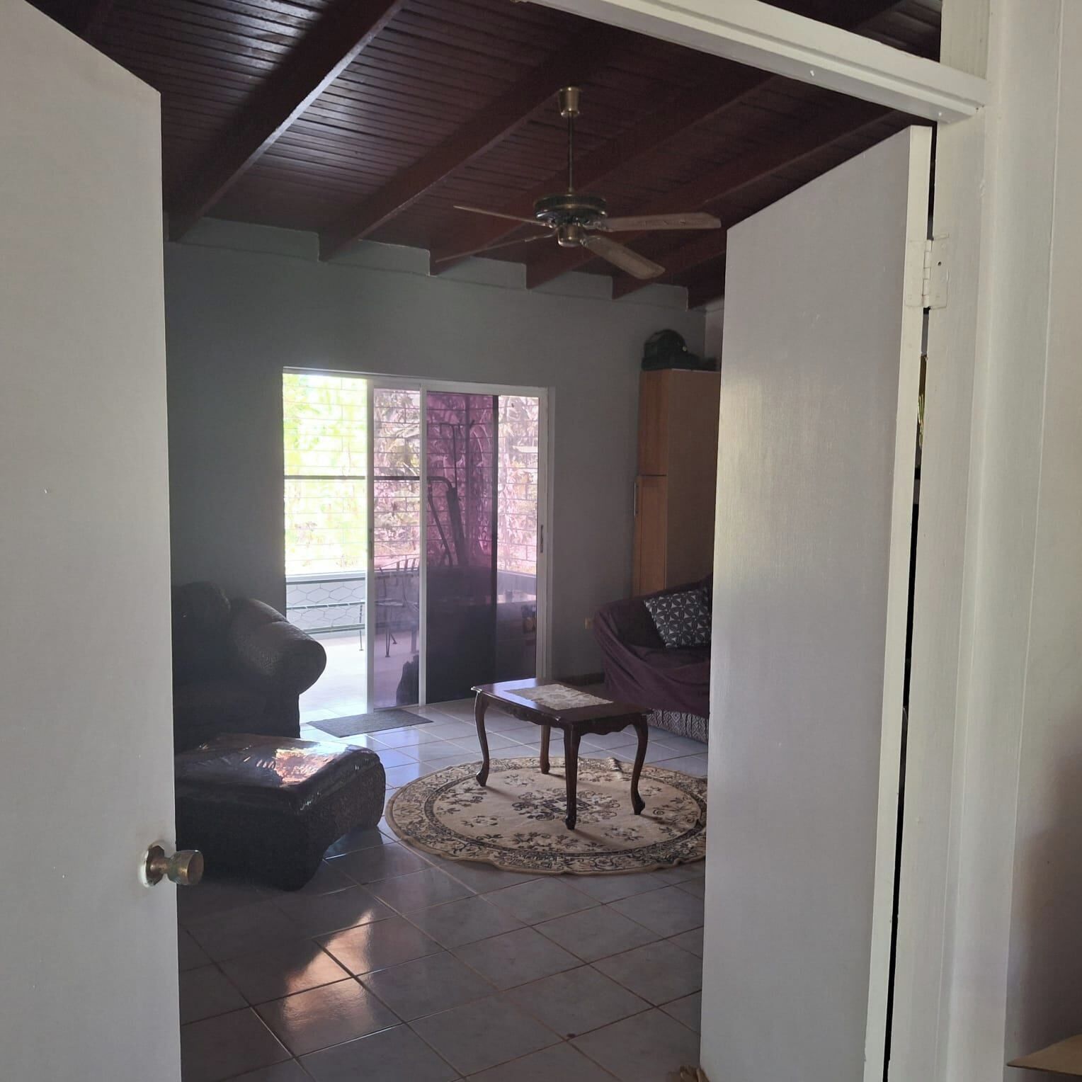 Una porta oberta a un saló amb un ventilador de sostre, un sofà, una taula baixa i una catifa amb dibuixos.