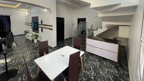 Une chambre d’hôtel moderne avec un sol en marbre, un coin repas avec une table blanche et des chaises marron, un escalier et un téléviseur fixé au mur.