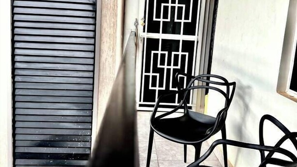 Ein Balkon mit zwei Stühlen, ein Fenster mit geometrischem Muster und eine Tür mit Lamellen.