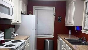 A compact kitchen with white cabinets, a stainless steel stove, a microwave, and a sink. - The Comic House (Clinton)