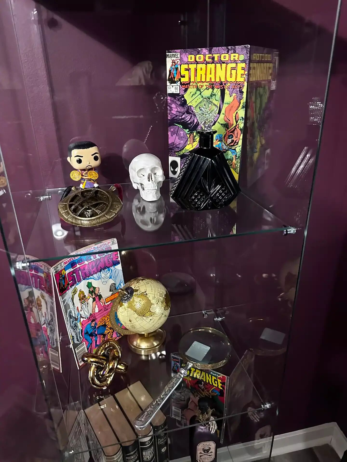 A glass display case with various collectibles, including a Doctor Strange comic, a skull, a globe, and figurines.