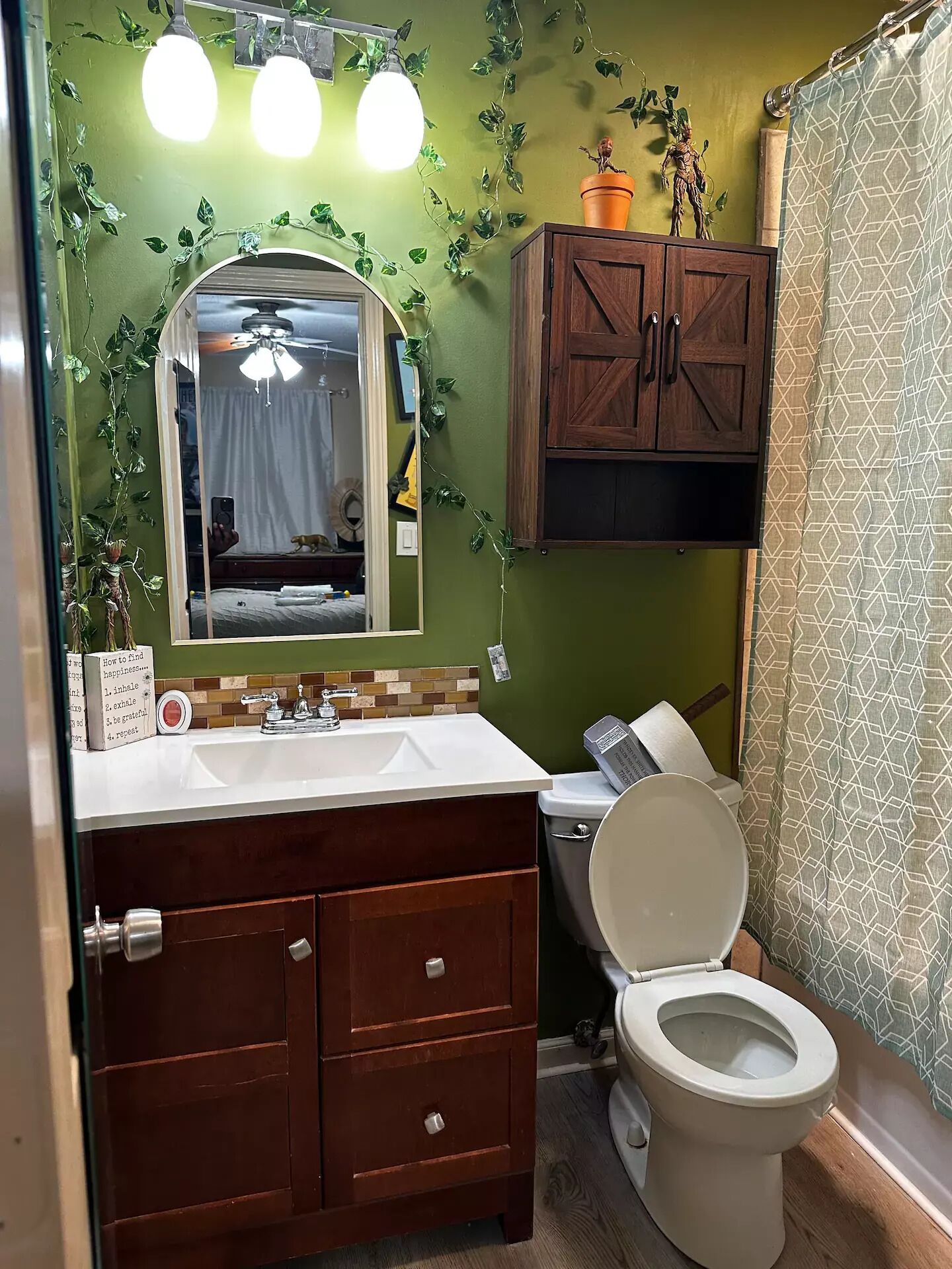Une salle de bain avec un mur vert, des meubles en bois, un lavabo blanc et des toilettes.