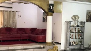 Una sala de estar con un sofá rojo, piso de mármol, un pilón decorativo y un estante con figuritas.