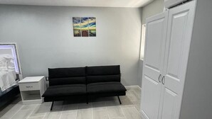 Un dormitorio con una cama, un sofá negro, un armario y una mesita de noche.