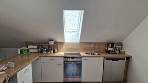 A compact kitchen with a dishwasher, stove, and sink. - Ferienwohnung Rebberg 2 – klimatisierte Unterkunft mit WLAN, Bergblick und Wallbox (Wolfach)