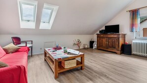A cozy living room with a red sofa, a wooden coffee table, a TV, and two skylights. - Ferienwohnung Rebberg 2 – klimatisierte Unterkunft mit WLAN, Bergblick und Wallbox (Wolfach)