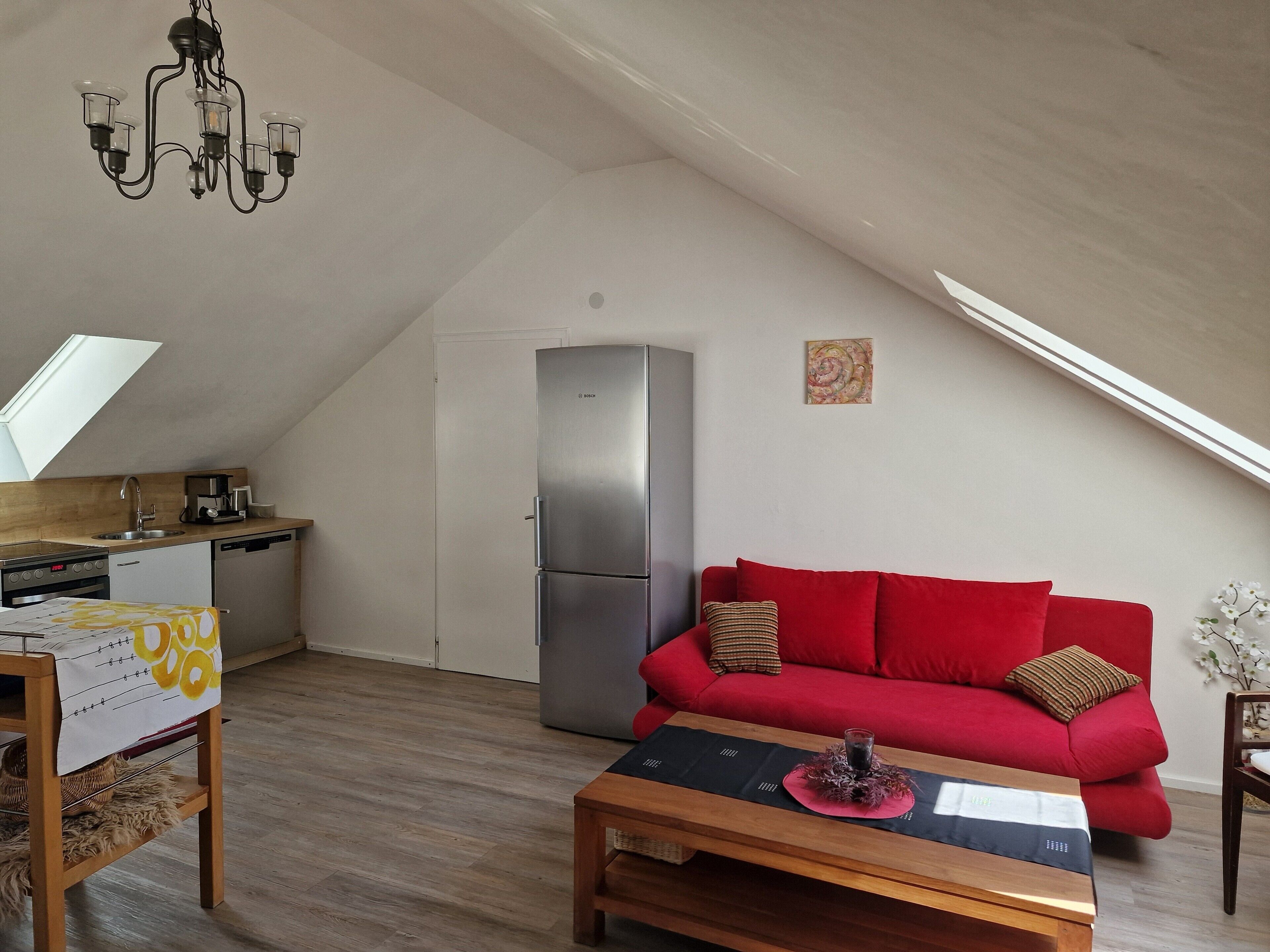 A modern loft with a kitchen, a red sofa, a wooden coffee table, and a chandelier.