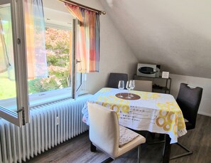Un comedor con una mesa, sillas, un ventanal con cortinas, un radiador y un microondas.