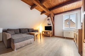 A cozy living room with a sofa, TV, wooden table, and a window with a view of a building.