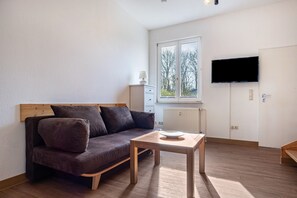 Un salon moderne avec un canapé, une table, un téléviseur et une fenêtre donnant sur des arbres.