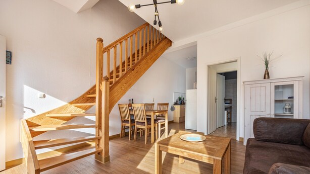 Una escalera de madera que conduce a un comedor con una mesa y sillas.