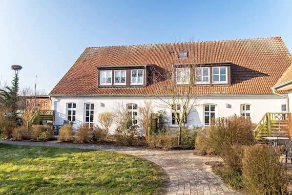 Une maison à deux étages, avec un toit recouvert de tuiles, un jardin à l’avant et un chemin menant à l’entrée.