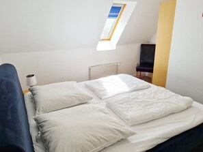 A bedroom with a bed, pillows, a lamp, a chair, a radiator, and a skylight. - Holiday Apartment 'Schwalbennest' with Terrace & Wi-Fi (Buchholz Müritz)