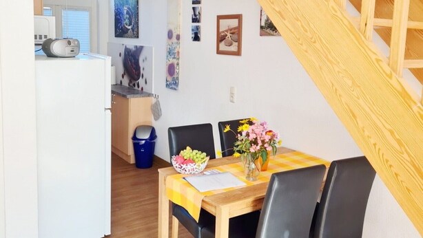 Un comedor con mesa de madera, sillas negras y un florero con flores.
