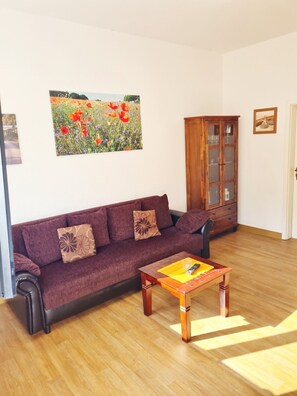 A living room with a sofa, a wooden cabinet, and a painting of a field. - Holiday Apartment 'Schwalbennest' with Terrace & Wi-Fi (Buchholz Müritz)