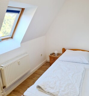A bedroom with a window, a radiator, a wooden floor, a bed, and a bedside table with a lamp. - Holiday Apartment 'Schwalbennest' with Terrace & Wi-Fi (Buchholz Müritz)