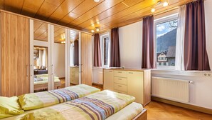 A bedroom with two beds, wooden ceiling, a radiator, and a window with curtains. - Apartment 'Michelskäppele' with Mountain View, Shared Terrace and Wi-Fi (Bad Urach)