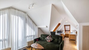 A modern loft with a high ceiling, a green sofa, a small table with a vase, and a view of the city through large windows. - Premium Apartment 'Hohenurach' with Mountain View, Shared Terrace and Wi-Fi (Bad Urach)