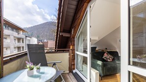 A balcony with a glass table, two potted plants, a green sofa, and a view of a mountain. - Premium Apartment 'Hohenurach' with Mountain View, Shared Terrace and Wi-Fi (Bad Urach)