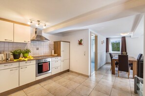Una cocina moderna con armarios blancos, una campana extractora de acero inoxidable y un comedor con mesa y sillas de madera.