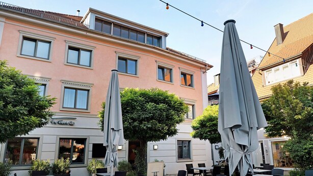 A building with multiple windows, outdoor seating with umbrellas, and a sign that reads 'Vamo.'
