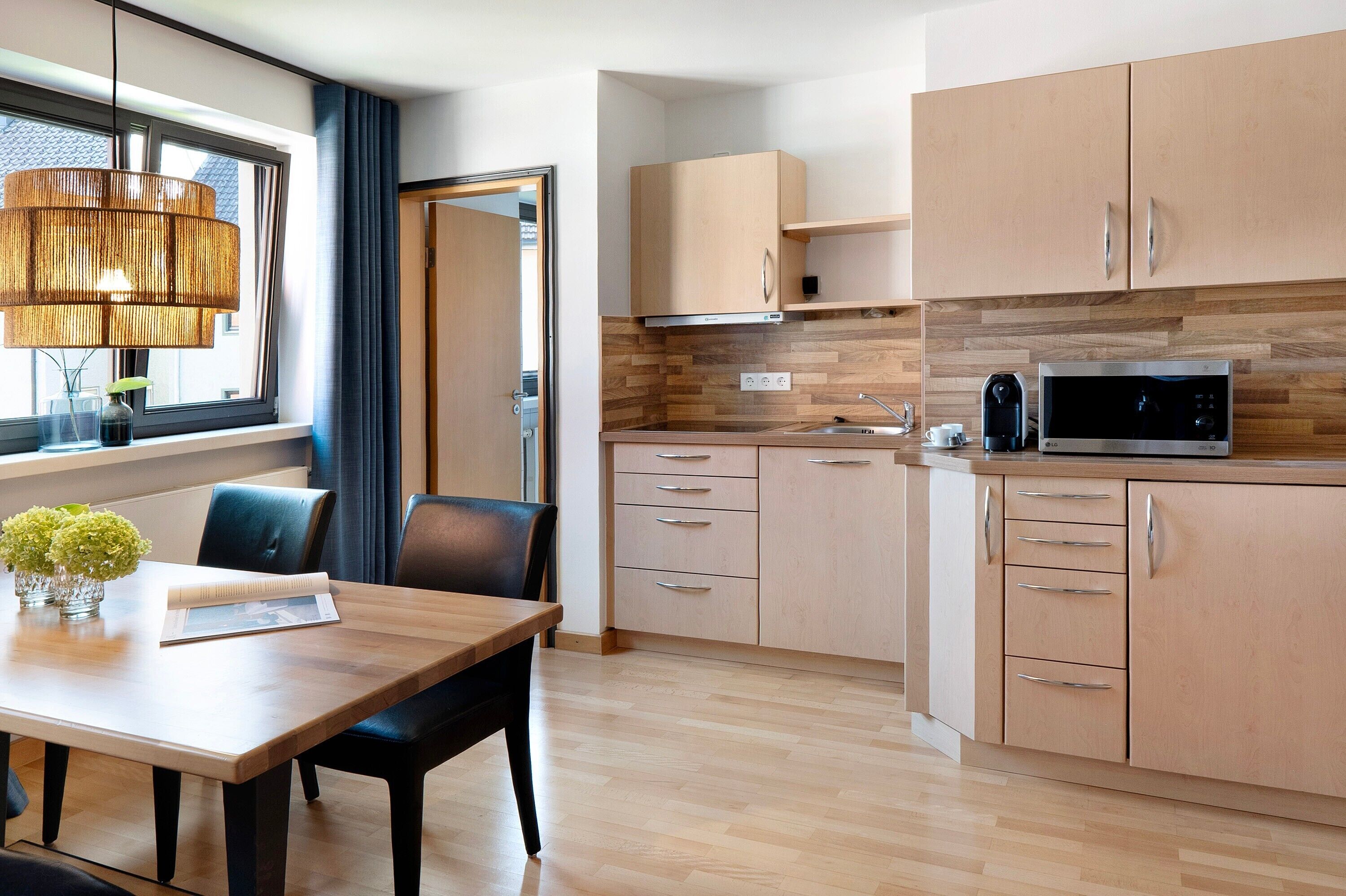 A modern kitchen with wooden cabinets, a microwave, and a dining area with a table and chairs.