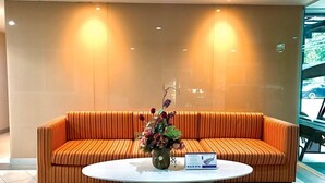 Un espace d’accueil avec un canapé orange à rayures, une table ronde blanche et un vase rempli de fleurs.