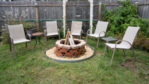 Un patio trasero con un pozo de fuego rodeado de sillas y una pérgola.