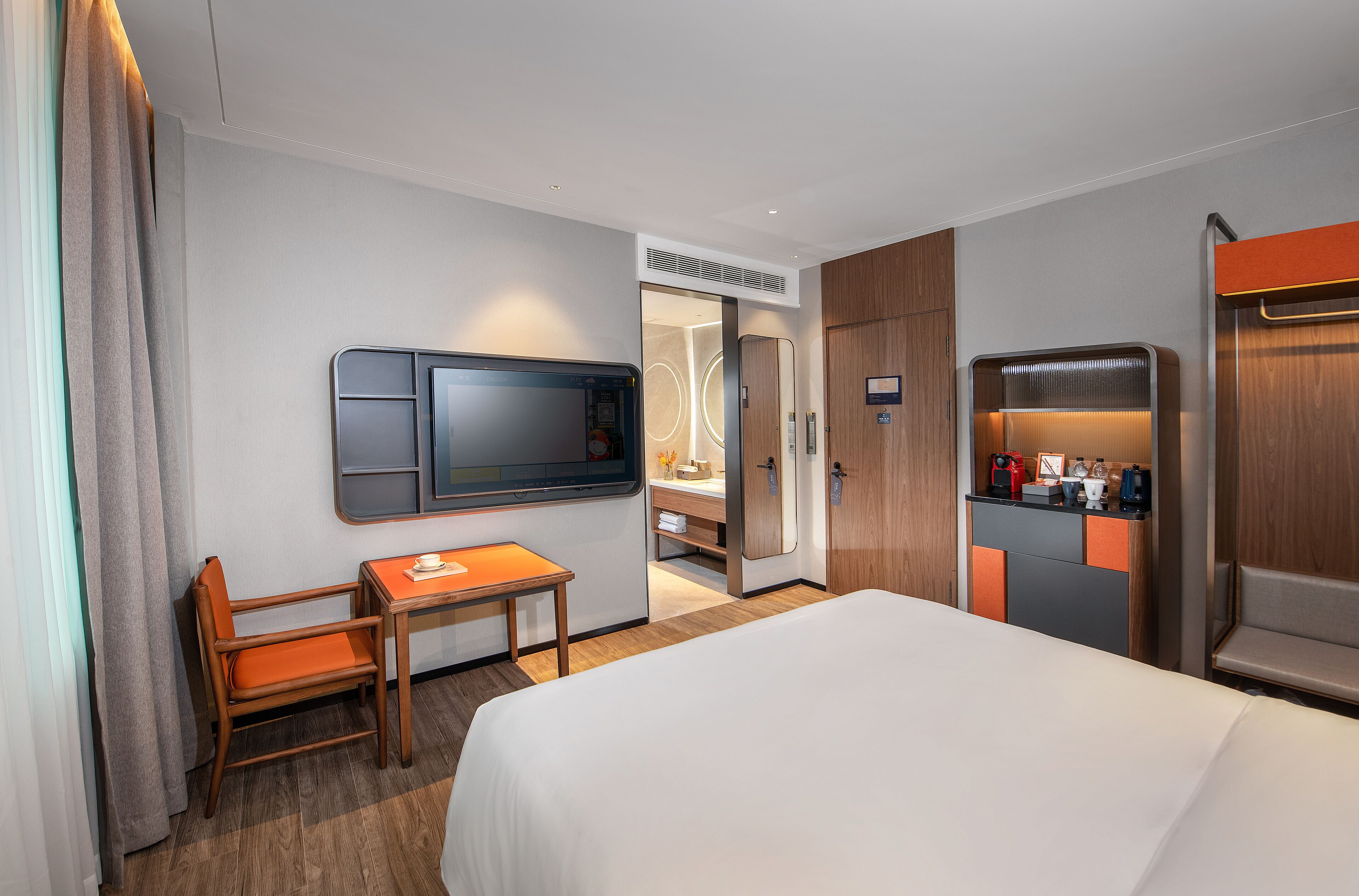 Una habitación de hotel con cama, escritorio, silla, televisor, minibar y baño.
