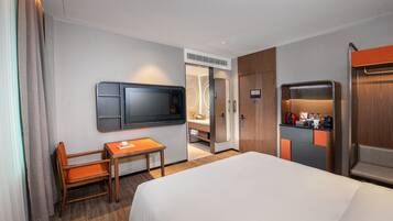 Una habitación de hotel con cama, escritorio, silla, televisor, minibar y baño.