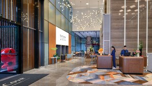 Eine moderne Hotelhalle mit einer Rezeption, einer Sitzecke und einem großen digitalen Bildschirm, der den Hotelnamen zeigt.