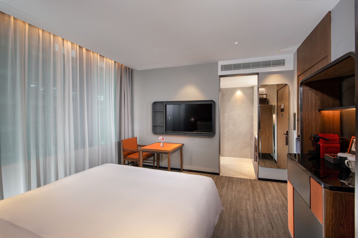 Une chambre d’hôtel avec un grand lit, un bureau, une chaise, une télévision et une kitchenette.