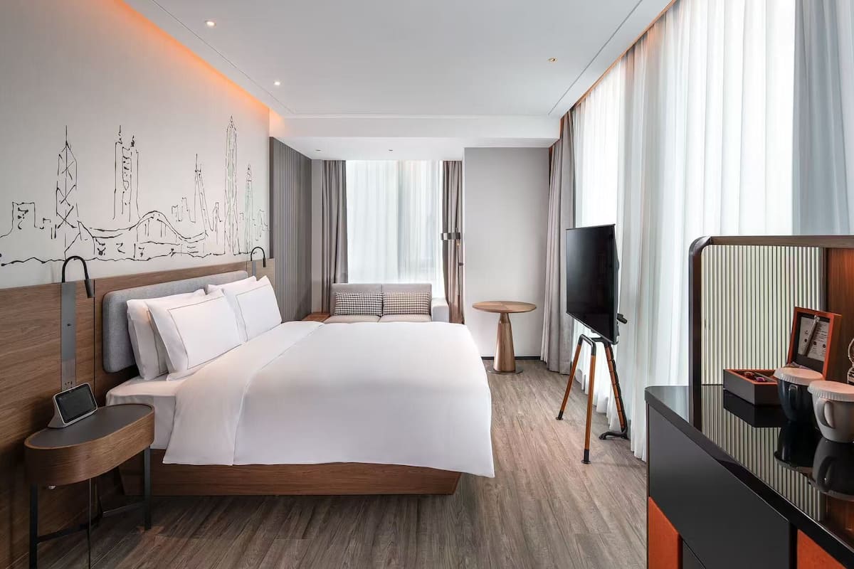A modern hotel room with a large bed, a television, a coffee machine, and a desk with a laptop.