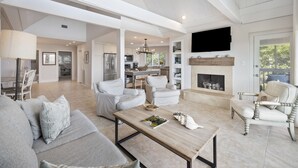 A spacious living room with a fireplace, modern furniture, and a kitchen in the background. - AMAZING Ocean Front View! Popular 3BR Seascape Condo! (Kiawah Island)