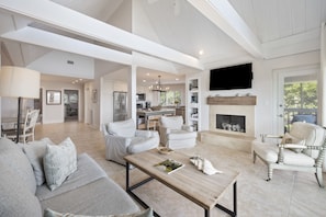 A spacious living room with a fireplace, modern furniture, and a kitchen in the background. - AMAZING Ocean Front View! Popular 3BR Seascape Condo! (Kiawah Island)
