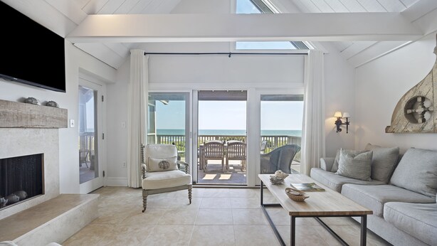 A spacious living room with a fireplace, a sofa, a coffee table, and a view of the ocean through large sliding doors. - AMAZING Ocean Front View! Popular 3BR Seascape Condo! (Kiawah Island)