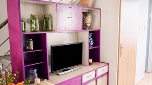 Ein Zimmer mit Fernseher auf einer Holzkabine, Regalen mit Gläsern und einer Vase, und einer Tür im Hintergrund.