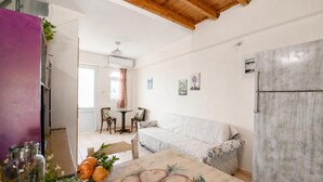 Ein gemütliches Wohnzimmer mit einer Couch, einem Esstisch mit floralem Tischläufer und einem Kühlschrank.