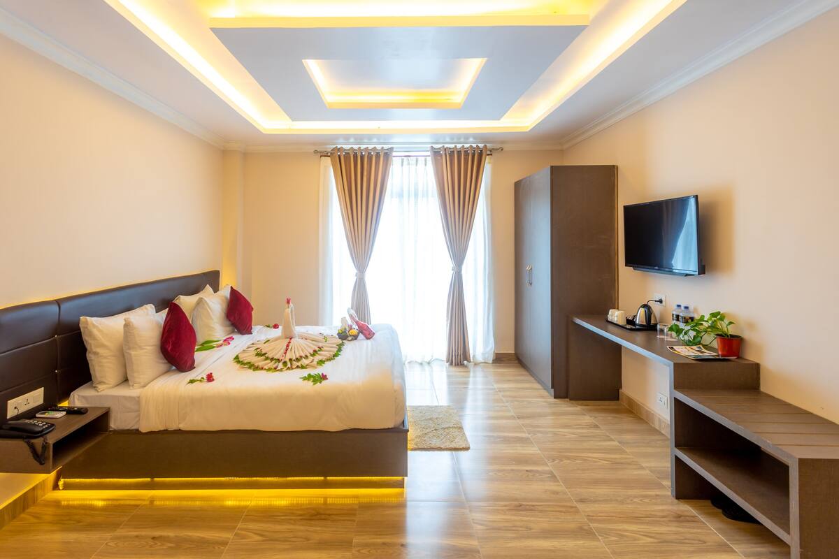 A modern hotel room with a large bed, a flat-screen TV, a desk, and a seating area.