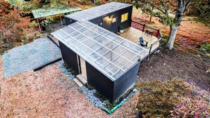 Un edificio moderno de dos pisos con techo plano, una pequeña terraza con asientos y una planta en maceta.