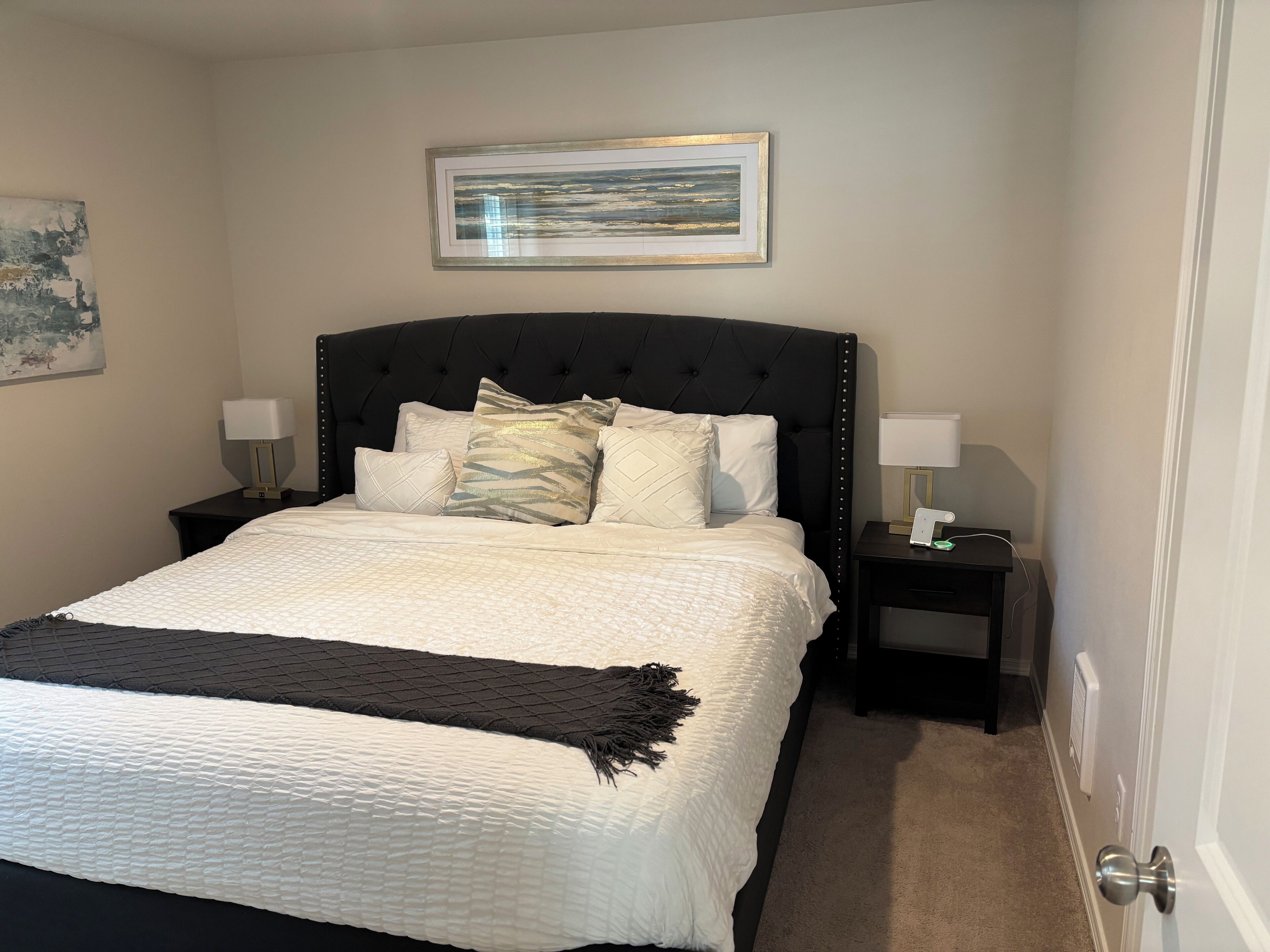 A neatly made bed with a black headboard, two bedside tables with lamps, and a framed picture on the wall.