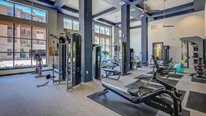 Een sportschool met diverse fitnessapparaten, grote ramen en uitzicht op gebouwen.