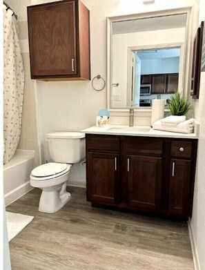 A bathroom with a toilet, a sink with a mirror, and wooden cabinets. - Frisco's mini Resort Stay
(Frisco)