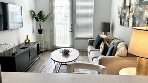 Een moderne woonkamer met een bank, een salontafel, een televisie en een schilderij aan de muur.